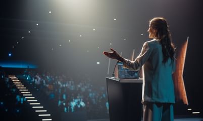 Excited Female Entrepreneur Shares an Insightful Talk on Technology and Leadership at a Professional Business Conference. Diverse Multiethnic Guests Sitting in a Dark Auditorium
